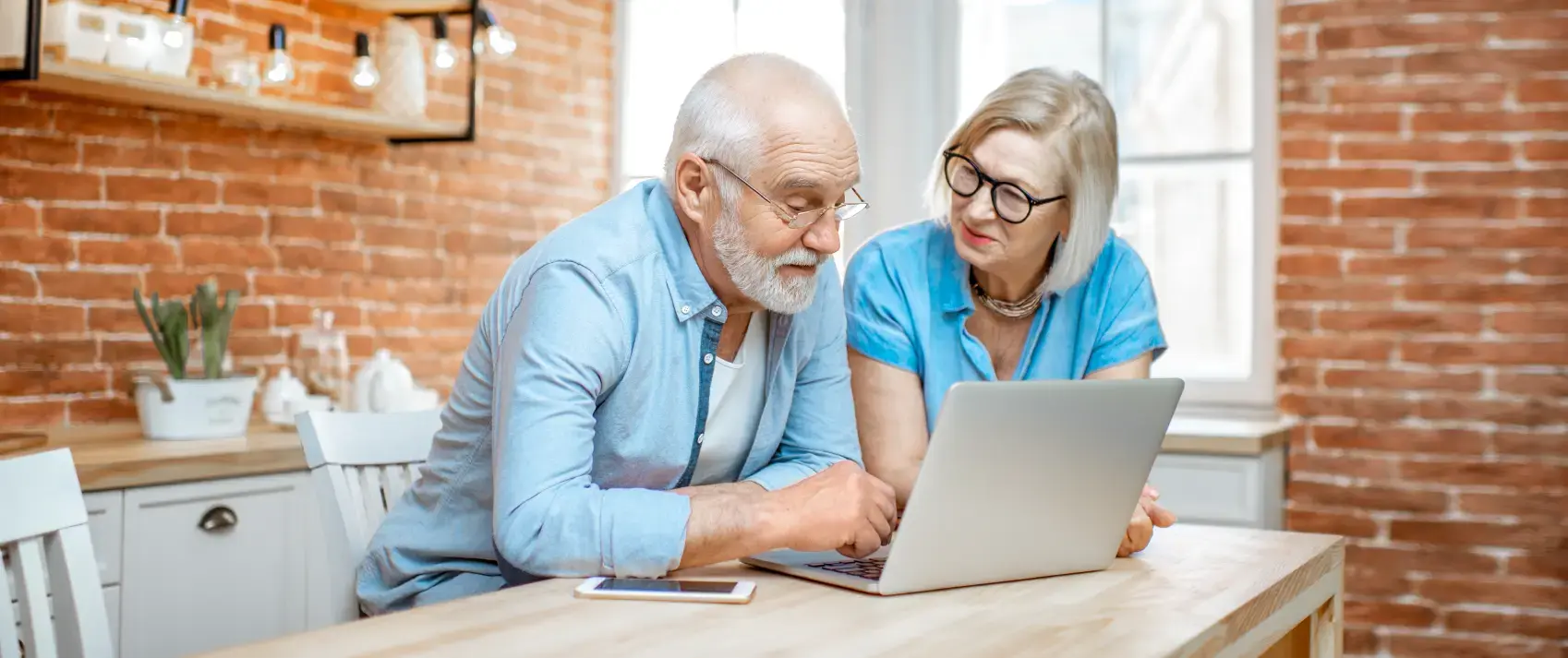 senior couple in blue shirts sitting together with laptop on the kitchen at home